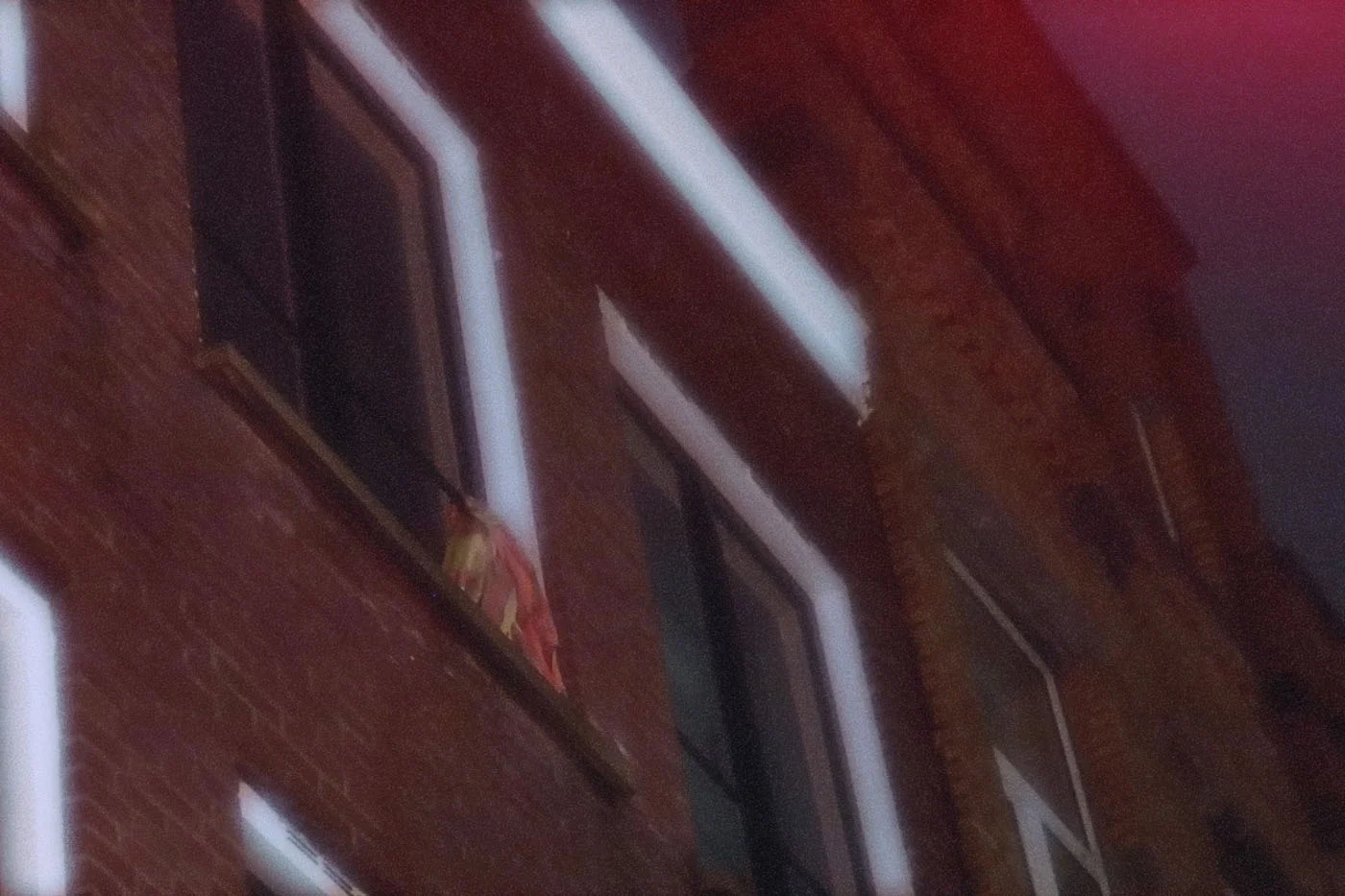 Zoomed in, grainy view of a window at night, lit my blue and red lamps.