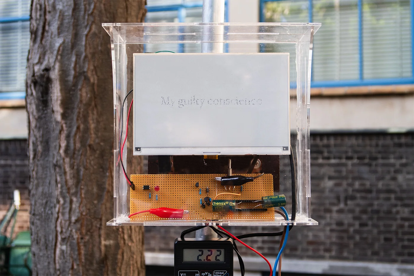 A circuit box and an electronic ink screen inside a transparent enclosure. On the screen, barely readable, one can see the leftovers of a faded message - my guilty conscience.